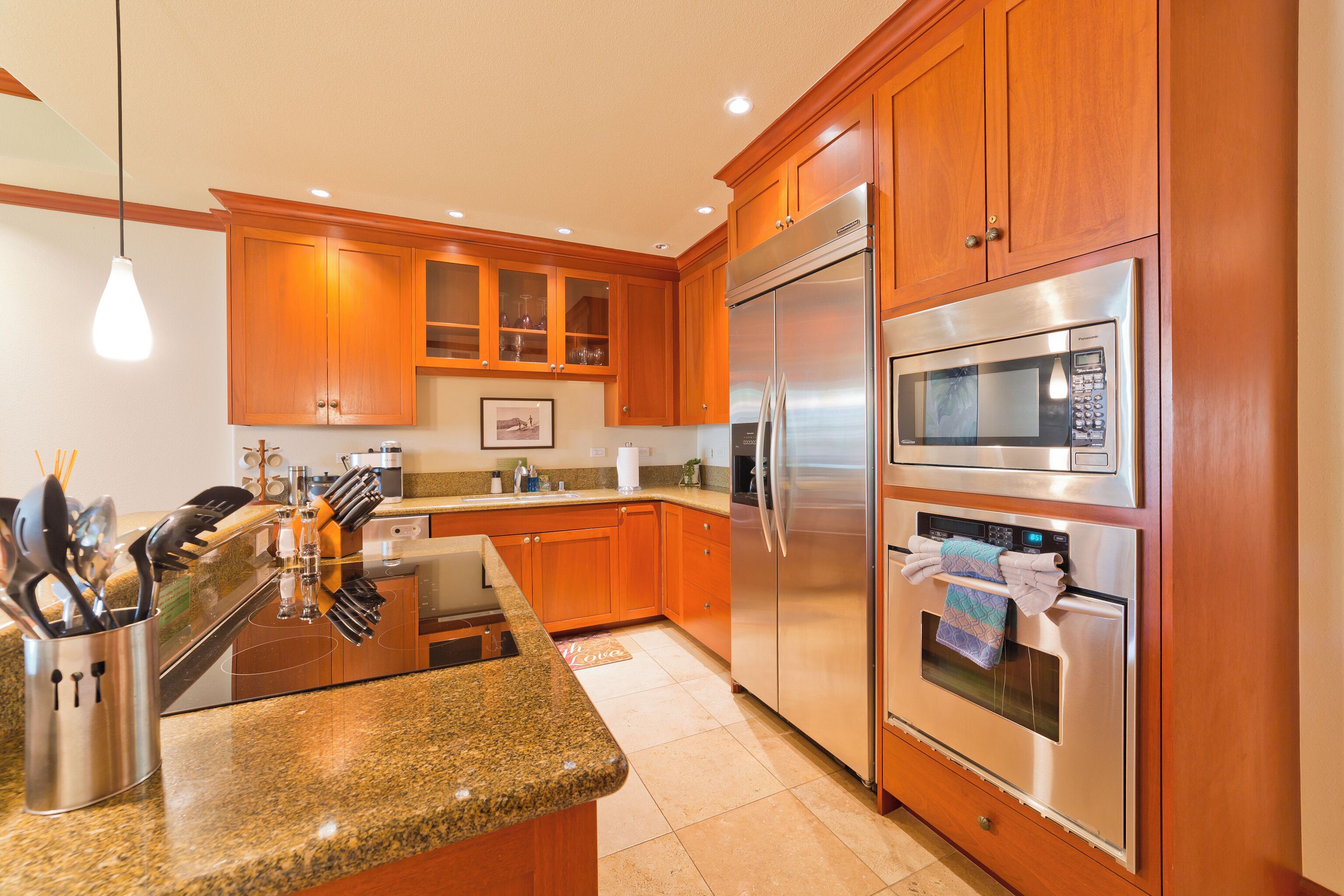 A modern kitchen with wooden cabinets, stainless steel appliances, granite countertops, and a hanging light fixture.