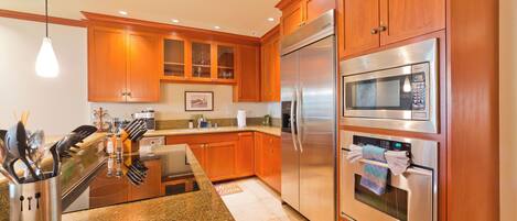 A modern kitchen with wooden cabinets, stainless steel appliances, granite countertops, and a hanging light fixture.