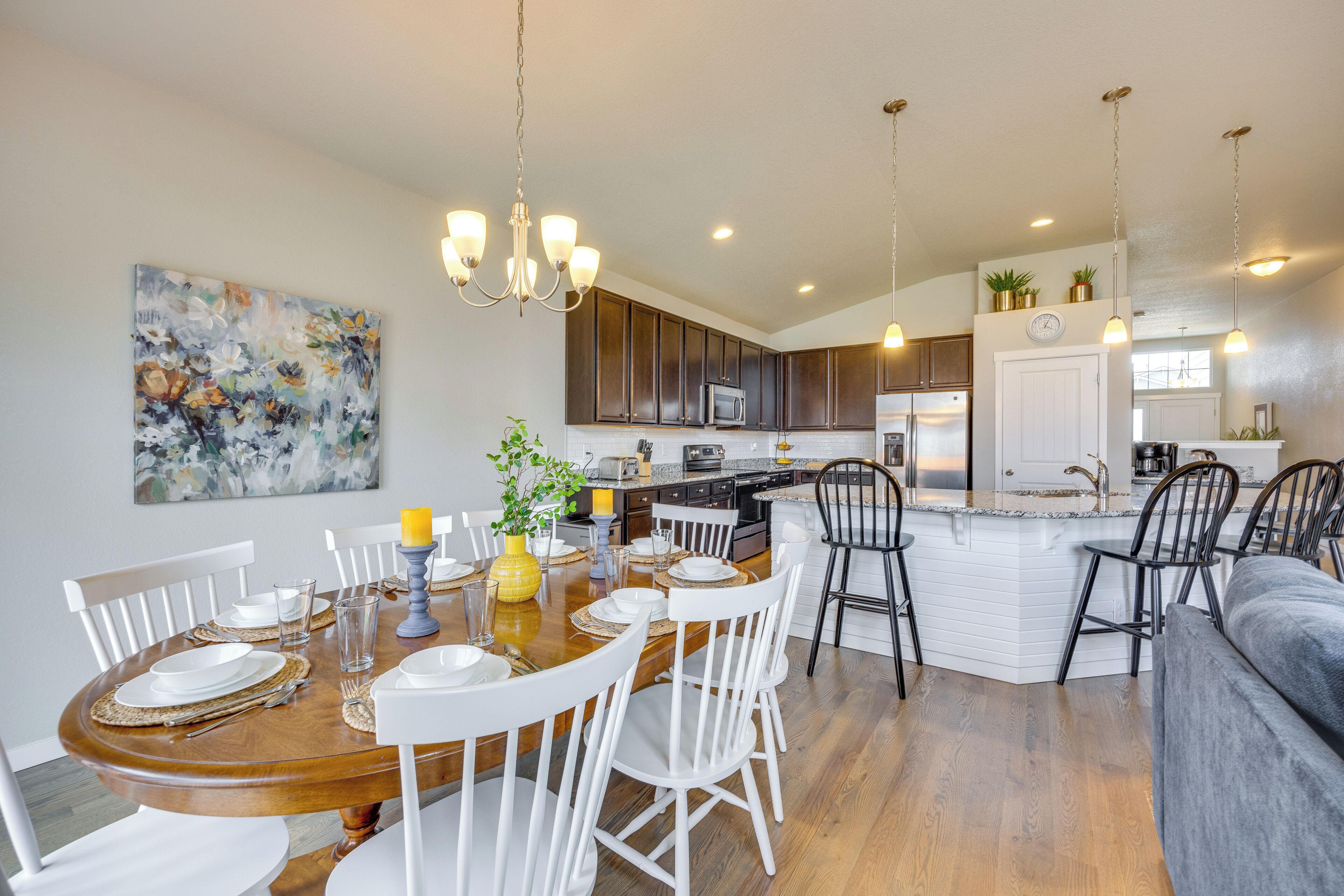 A modern kitchen with dark cabinets, a central island, and a dining area with white chairs and a wooden table.