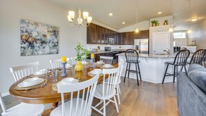 A modern kitchen with dark cabinets, a central island, and a dining area with white chairs and a wooden table. - Stunning Peyton Retreat w/ Game Room, Private Yard (Peyton)