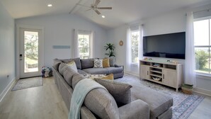 Ein geräumiges Wohnzimmer mit einem großen grauen Ecksofa, einem Flachbildfernseher und einem Deckenventilator.