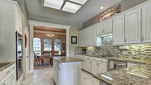 A kitchen with white cabinetry, granite countertops, and a stone backsplash. There is a dining area with a chandelier and large windows. - Come see why Granbury is Texas' best kept secret! Unwind at La Paloma - Enjoy!  (Granbury)