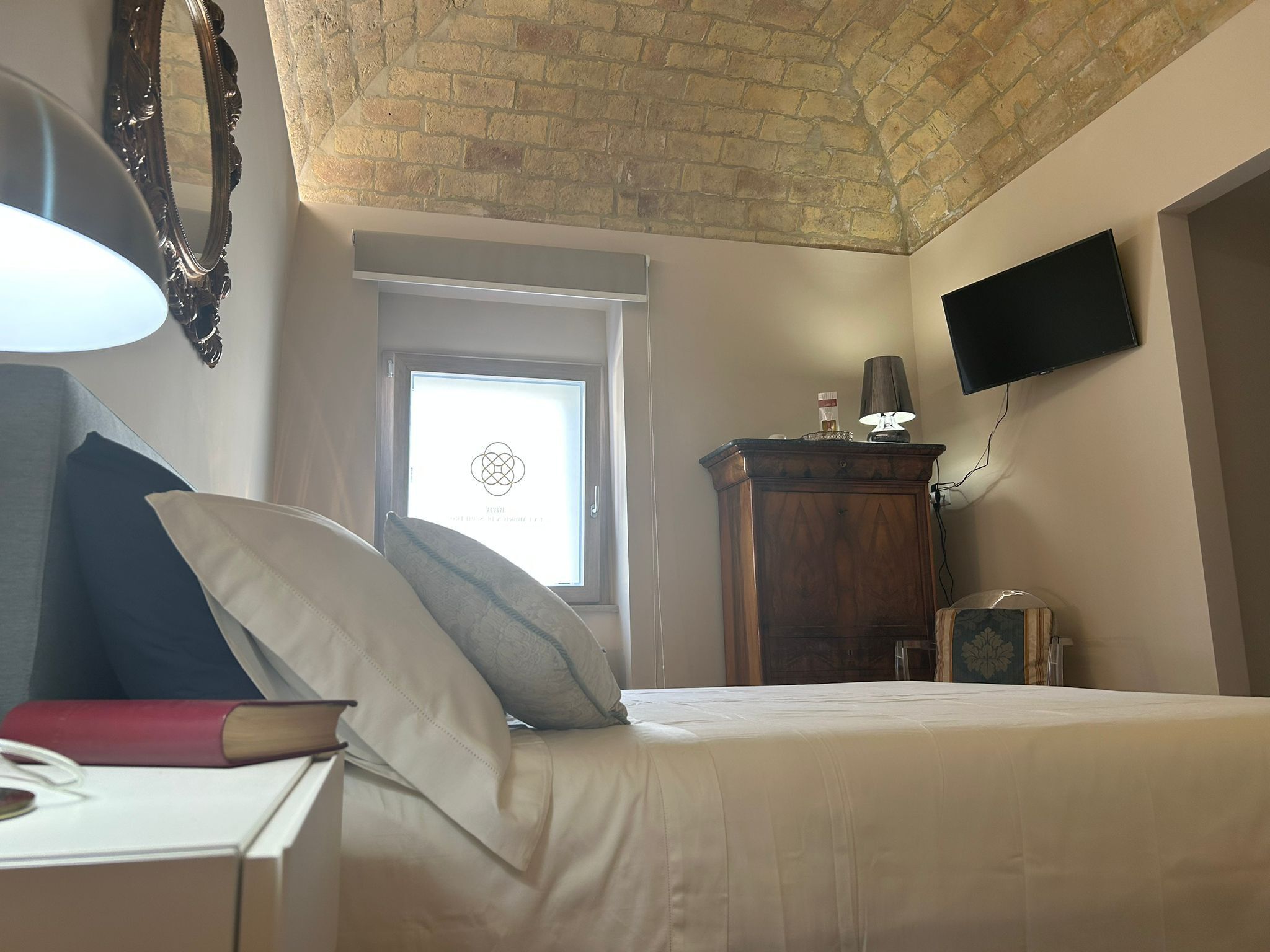 Une chambre à coucher avec un lit, un bureau avec une lampe, un téléviseur fixé au mur et une fenêtre donnant sur le ciel.