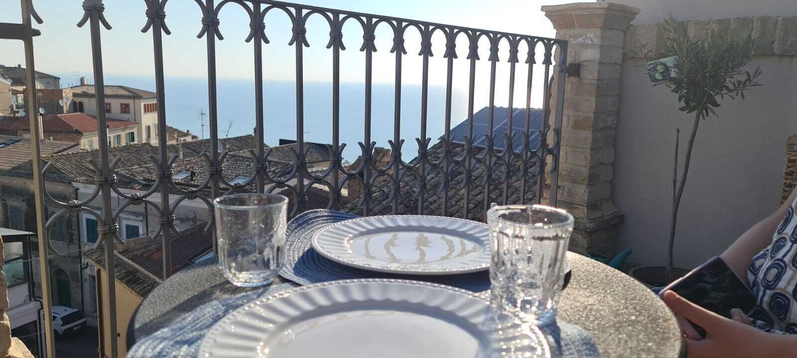 Un balcón con una mesa dispuesta para dos personas, con vista a un pueblo costero.