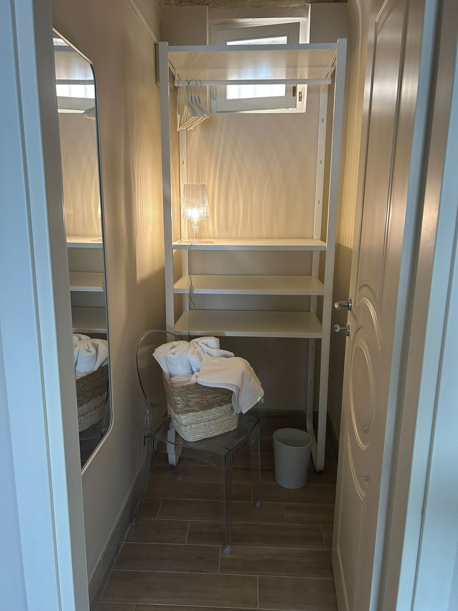Une petite pièce comprenant un lit superposé, une petite table avec une lampe, un panier en osier et une poubelle.