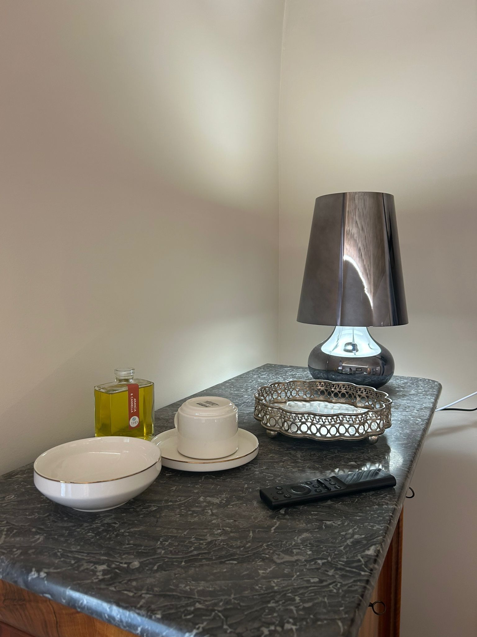 A kitchen counter with a marble top, a white ceramic cup, a remote control, a decorative tray, and a bottle of oil.
