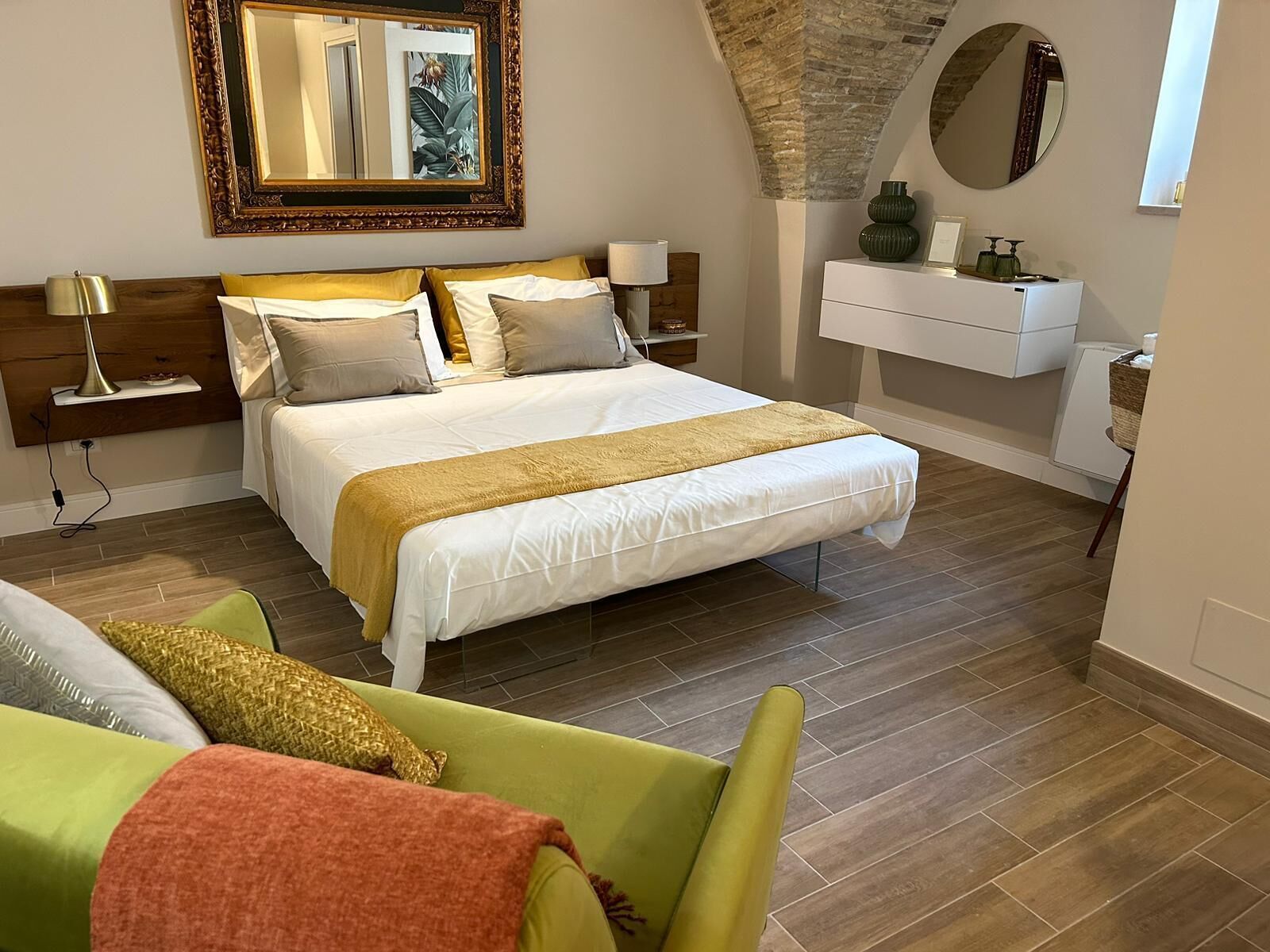 A bedroom with a large bed, a nightstand, a dresser, a mirror, and a green armchair.