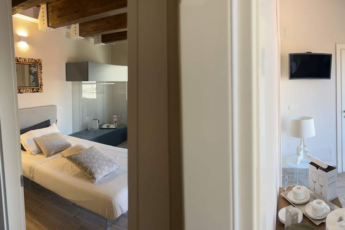 A modern hotel room with a bed, a sofa, a TV, and a dining area with a table set for two.
