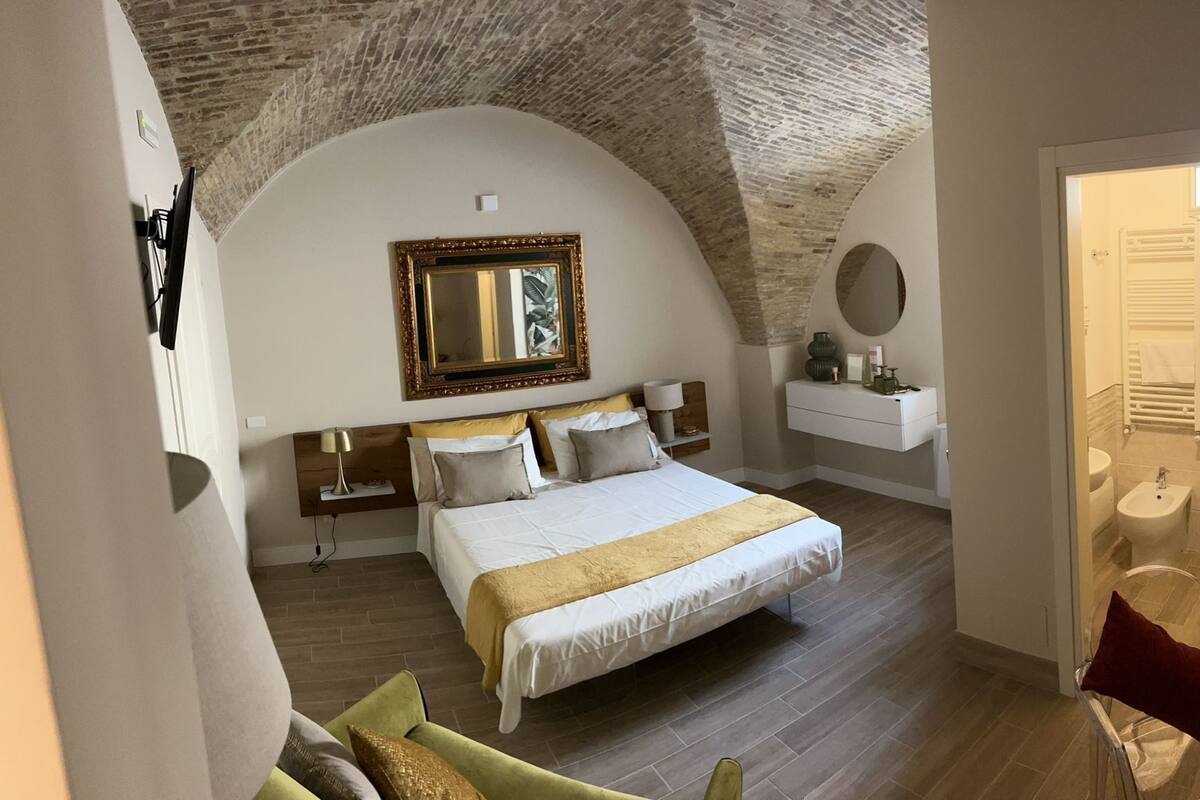 A bedroom with a large bed, a mirror, a bedside table, and a nightstand.