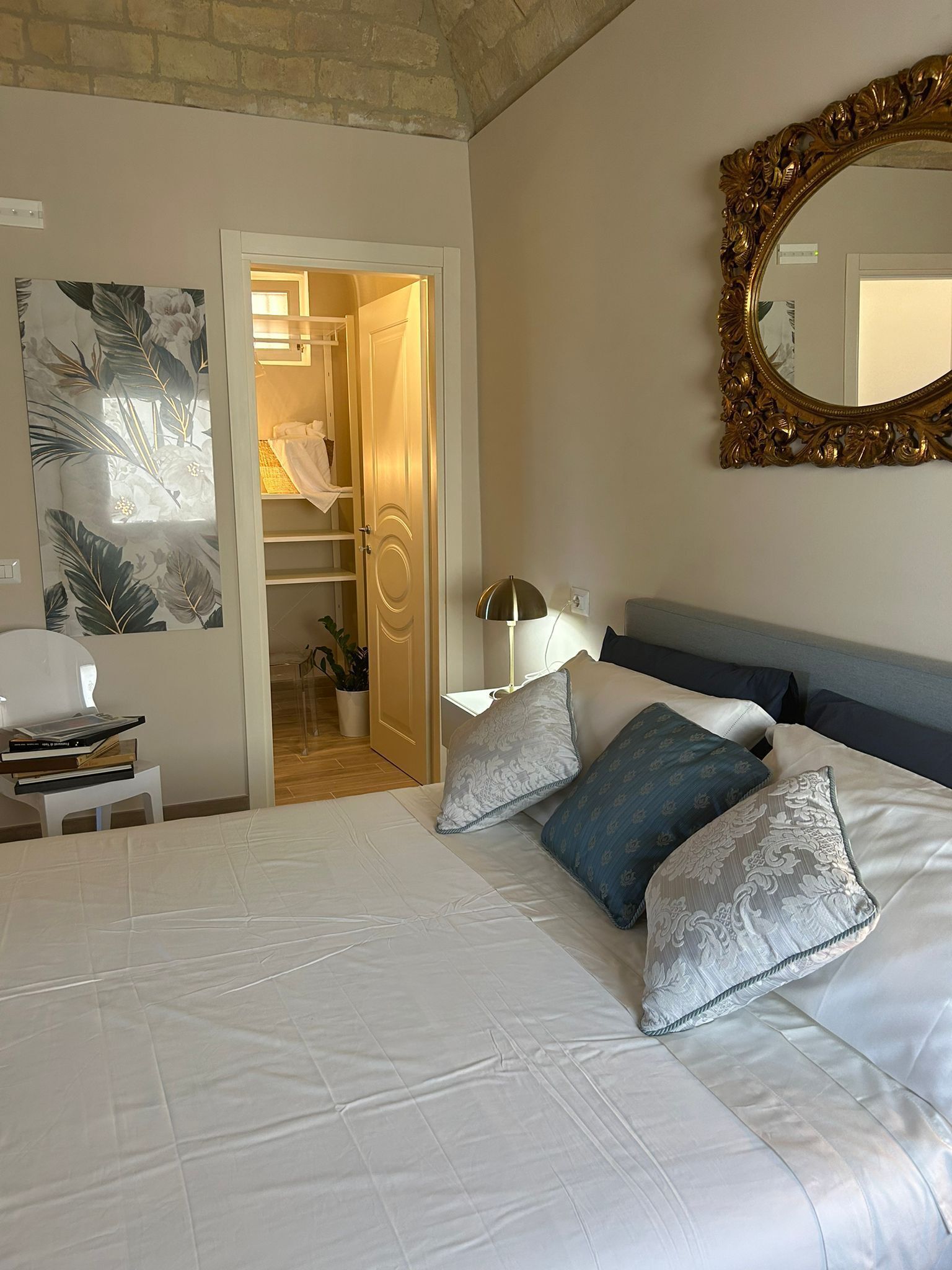 Une chambre avec un grand lit, une armoire, un miroir et un mur orné d’un tableau représentant des motifs floraux.