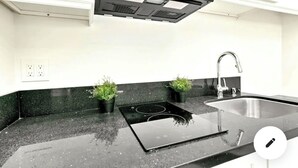 A kitchen with a black countertop, a stainless steel sink, and two potted plants. - Stylish Studio Center of North Park  (San Diego)