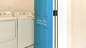 A laundry room with a blue door labeled "Laundry Room" and two white washing machines. - Stylish Studio Center of North Park  (San Diego)