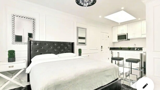 A modern bedroom with a large bed, a bedside table, a mirror, and a chandelier. - Stylish Studio Center of North Park  (San Diego)
