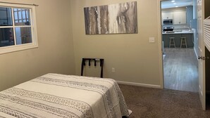 Ein Schlafzimmer mit einem Bett, einem Deckenventilator, einem Fenster und einer Tür, die in eine Küche führt.
