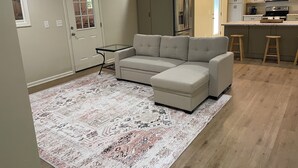 Eine moderne Küche mit Einbauofen, Mikrowelle und Kühlschrank. Es gibt ein beiges Modulsofa und einen kleinen Glastisch.