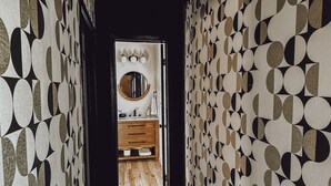 Ein Flur mit strukturierter Tapete, Holzboden sowie ein Badezimmer mit Spiegel, Waschbecken und Holzschrank.