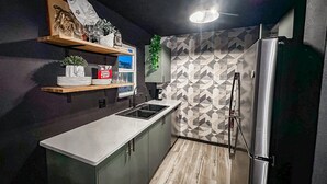 Eine kleine Küche mit integriertem Spülbecken, einem Kühlschrank und einem Regal mit Dekoration.