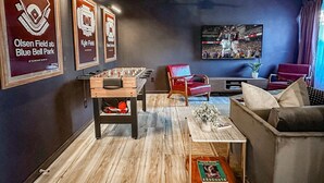 Ein Wohnzimmer mit Kicker, einem roten Sessel, einer Couch und einem Fernseher an der Wand.
