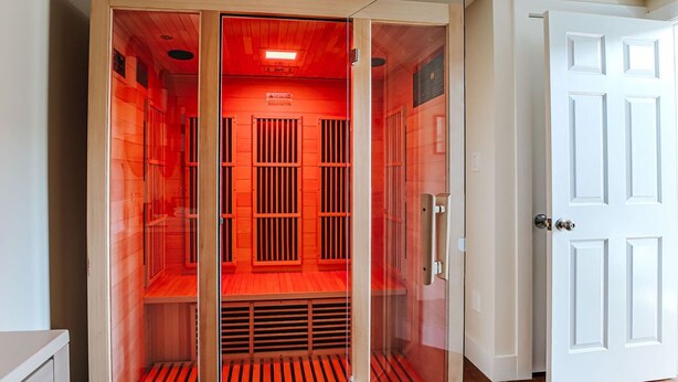 Ein begehbarer Kleiderschrank mit Glaswänden, roter Innenausleuchtung, einer weißen Tür und Holzboden.