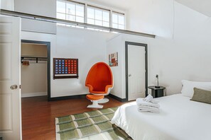 Une chambre d’hôtel avec un lit, une chaise, une œuvre d’art murale et une porte.
