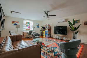 A living room with a sofa, armchair, TV, ceiling fan, and decorative items.
