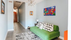 Een moderne woonkamer met een groene bank, een kleurrijk abstract schilderij en een trap naar een andere kamer.