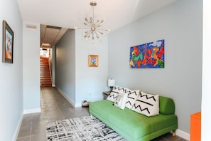 A modern living room with a green sofa, a colorful abstract painting, and a staircase leading to another room.