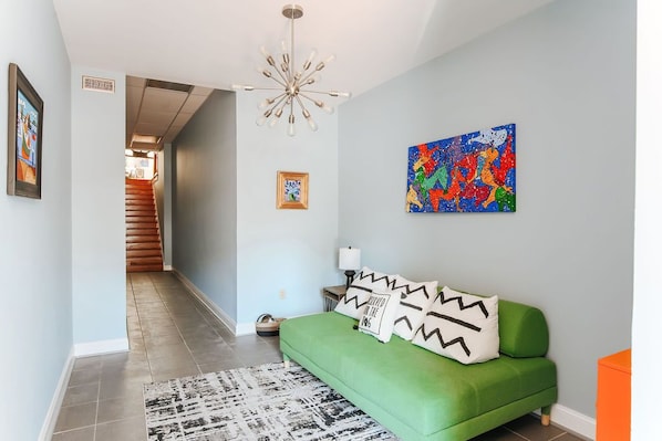 Una sala de estar moderna con un sofá verde, un cuadro abstracto colorido y una escalera que lleva a otra habitación.