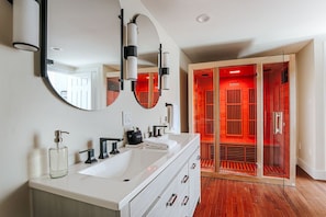 Een moderne badkamer met een wit wastafelmeubel, een grote spiegel en een inloopkast met rode verlichting.