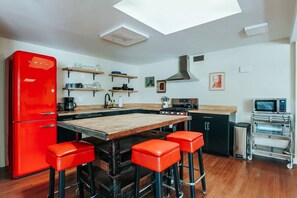 A compact kitchen with a red refrigerator, wooden bar stools, a microwave, and a small oven.