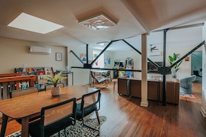 A spacious living area with a wooden dining table, black chairs, a potted plant, and a modern entertainment unit with a flat-screen TV.