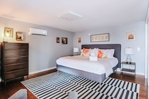 Een moderne slaapkamer met een groot bed, een dressoir, een nachtkastje en een wandairconditioner.