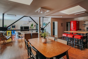 Een ruime woonkamer met een houten eettafel, rode barstoelen en een groot raam met uitzicht op een stadsbeeld.