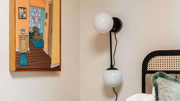 Een hotelkamer met een bed, een nachtkastje, een wandlamp en een lijst met een afbeelding van een kamer.