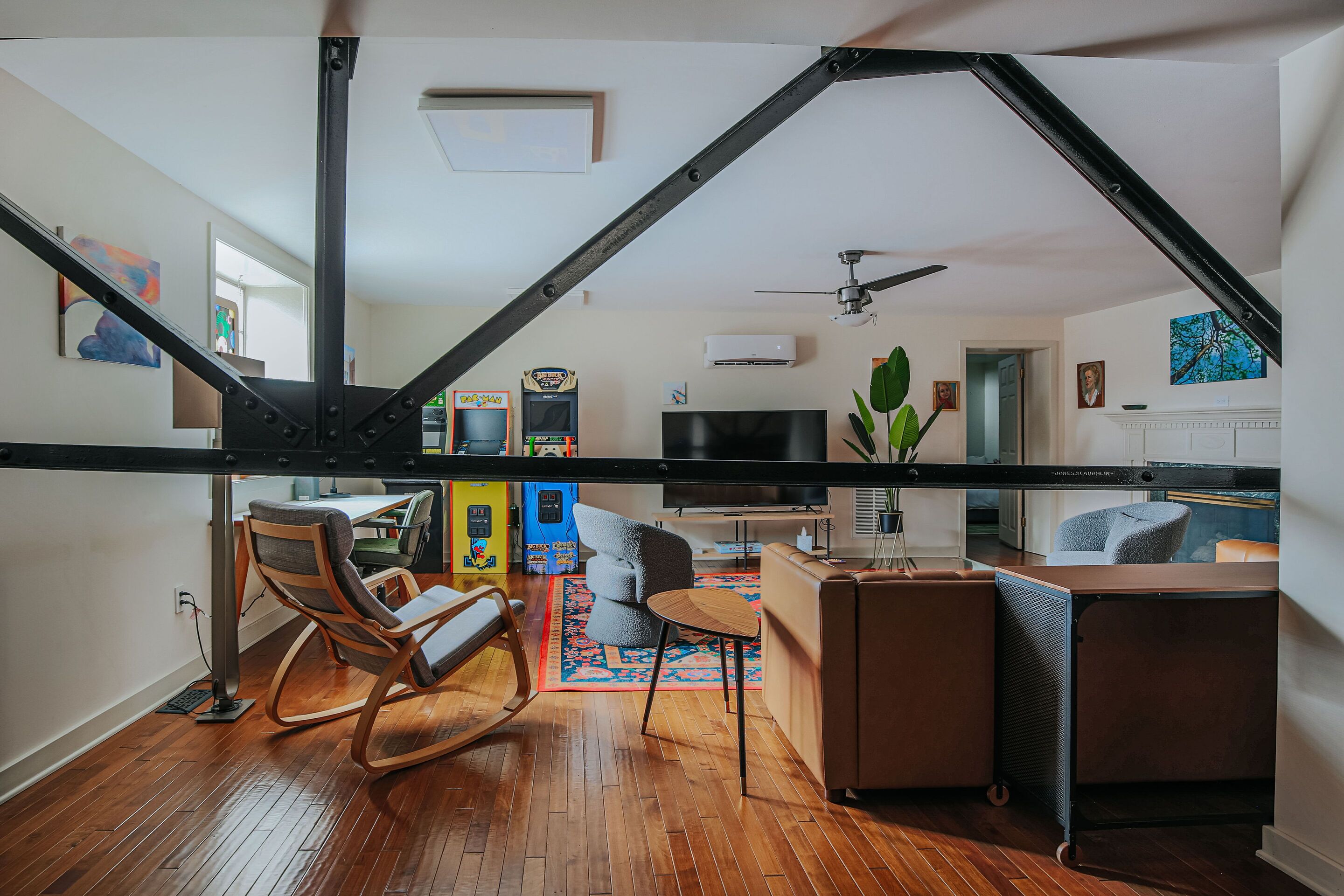 A modern loft apartment with exposed structural beams, a wooden floor, a dining area, a living room with a TV, and a staircase.