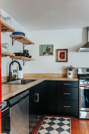 Una cocina moderna con armarios negros, encimera de madera, lavavajillas, estufa y dos cuadros en la pared.