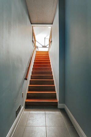A staircase with wooden steps and a metal handrail, leading to an open area with natural light.