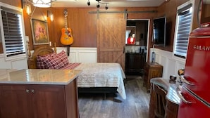 A compact room with a bed, a small kitchen area, and a red appliance. - Something to Write Home About @ The Wild West 40  (Cane Beds)