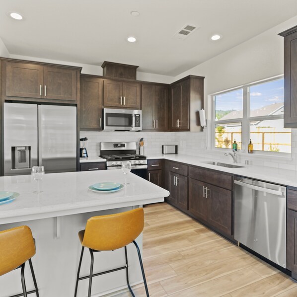 A modern kitchen with dark wooden cabinets, stainless steel appliances, and a large island with bar stools. - Newly Built Murphy's Modern Retreat (Murphys)