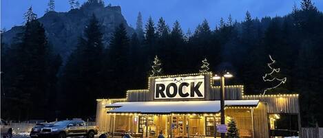 A building with a 'ROCK' sign, surrounded by trees and a mountainous backdrop.