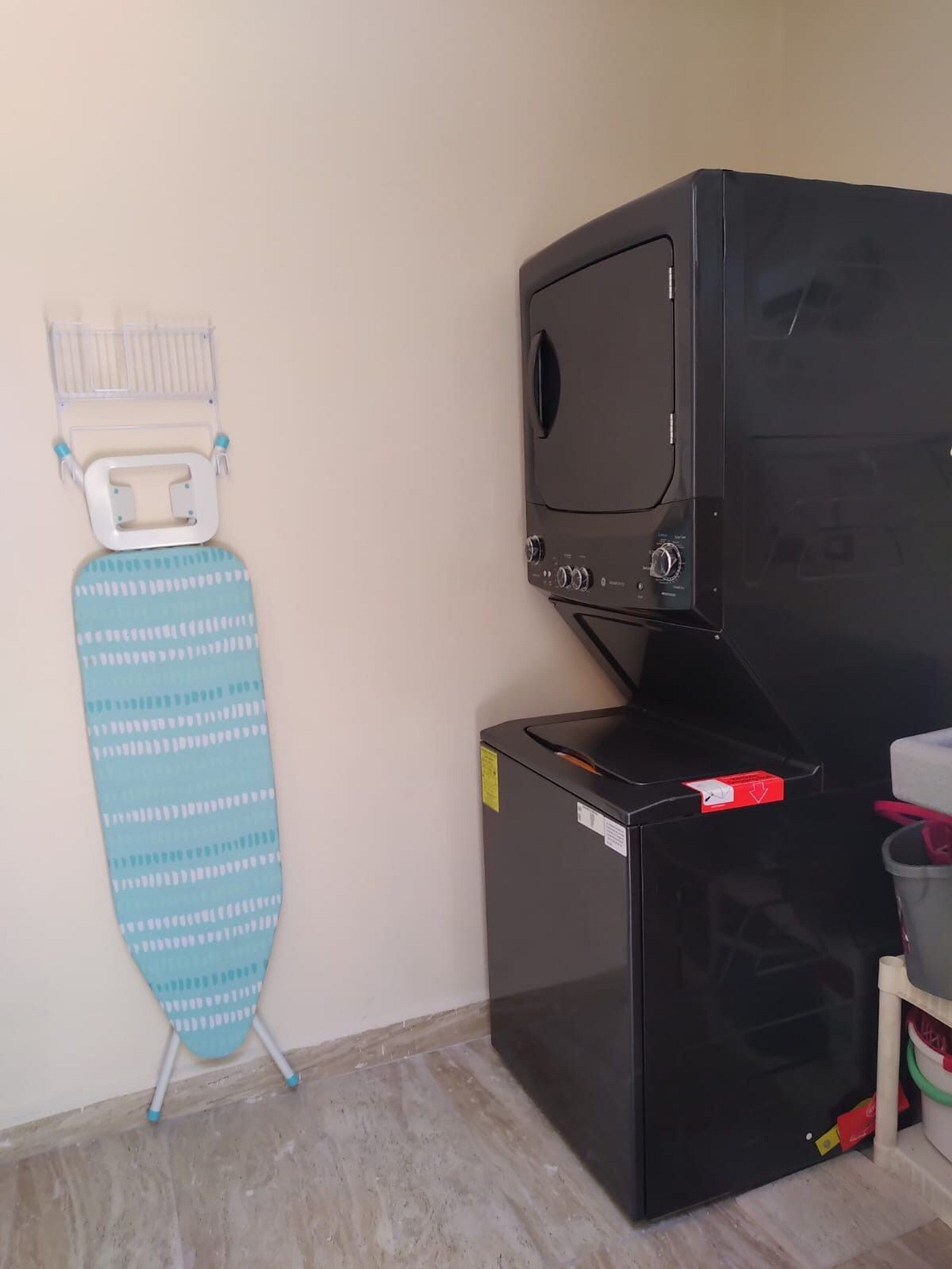 A compact black appliance, possibly a washer or dryer, next to a blue ironing board with a white base and teal legs.