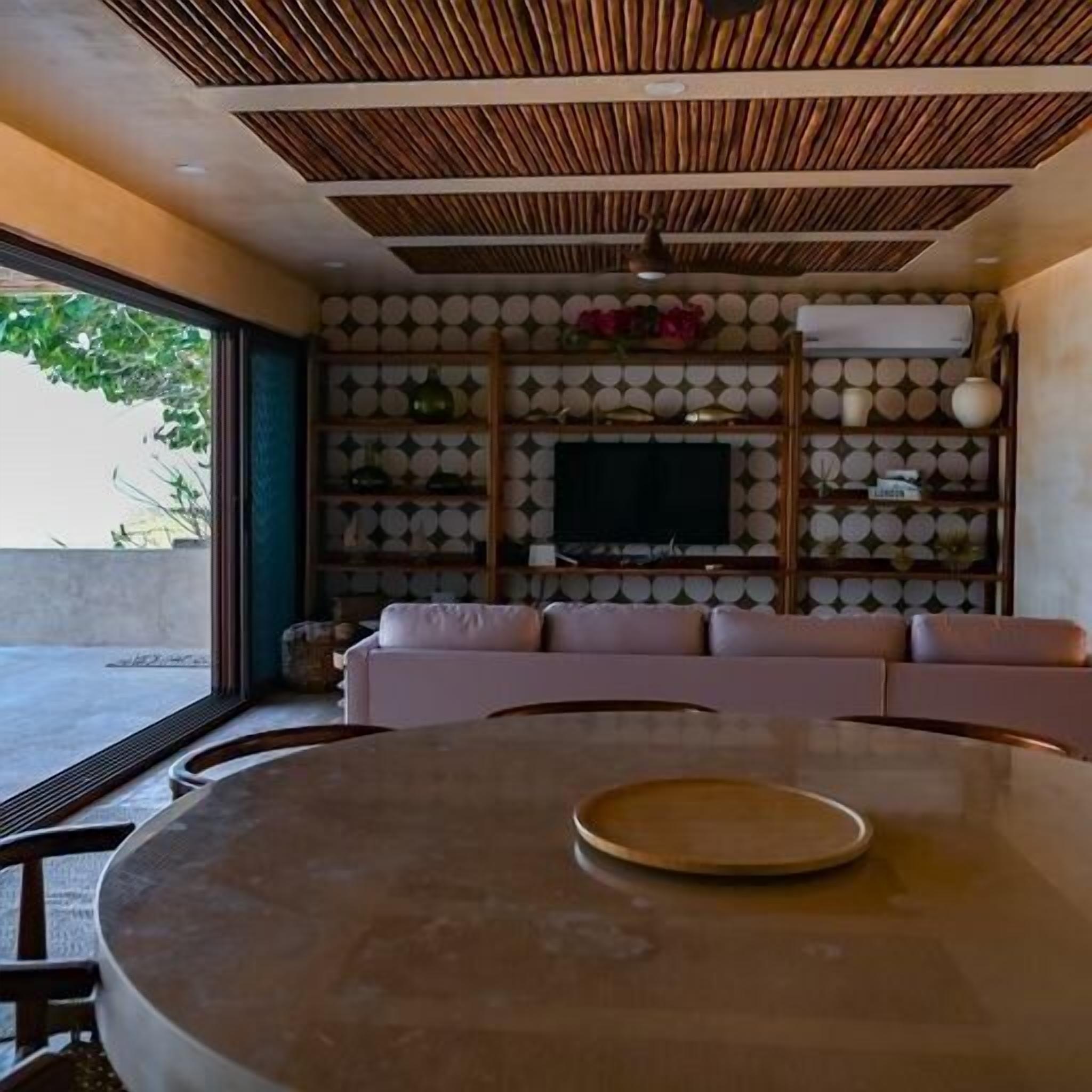 Una sala de estar moderna con una mesa redonda, un sofá rosa y un televisor sobre una pared con estantes decorados.