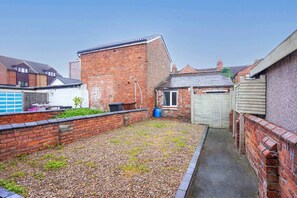 A courtyard with a gravel path, brick walls, and a small door leading to a garage.