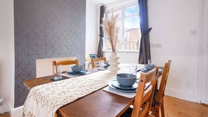 Un coin repas avec une table en bois, des chaises, un vase et une fenêtre avec des rideaux.