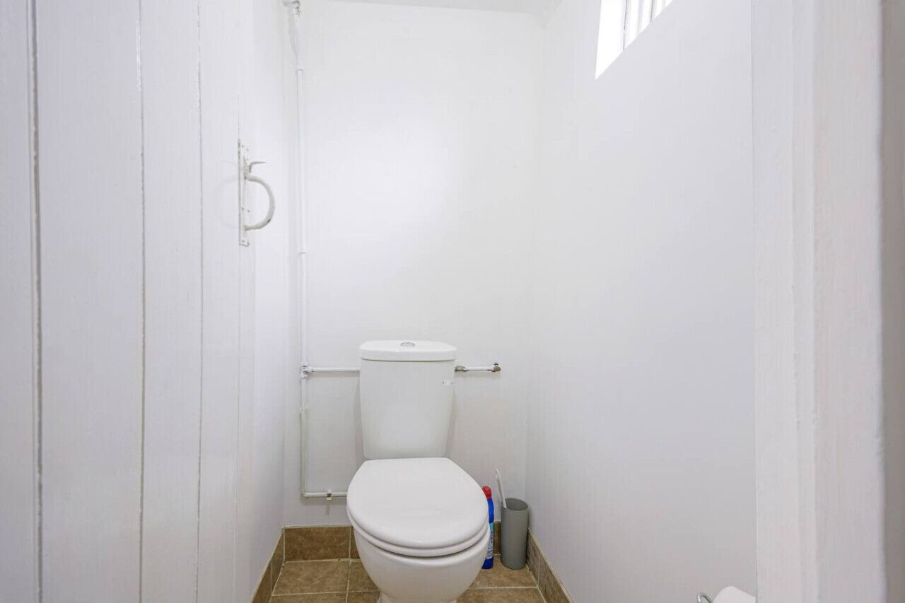 Un baño pequeño y blanco con inodoro, cortina de ducha y cubo de basura.