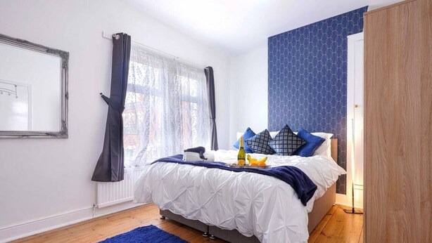 Une chambre à coucher avec un lit, un tapis bleu, une fenêtre avec des rideaux et un mur à motifs.