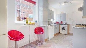 Une cuisine de taille réduite, équipée d’un lave-linge, d’un évier et d’une fenêtre avec un store rouge.