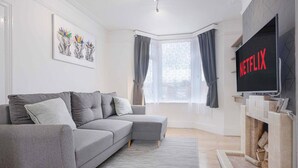 Un salon moderne avec un canapé d’angle gris, un téléviseur à écran plat, une cheminée et une grande fenêtre avec des rideaux.