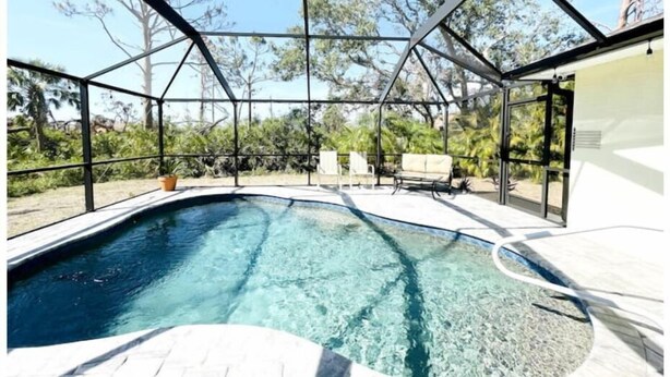 Une piscine dotée d’une structure en verre, entourée d’un espace extérieur aménagé avec des sièges et de la verdure.