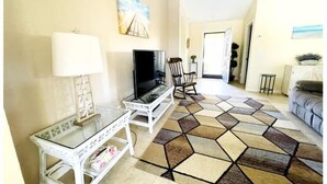 Un salon avec un téléviseur, une table en verre, un fauteuil à bascule et un tapis à motifs.